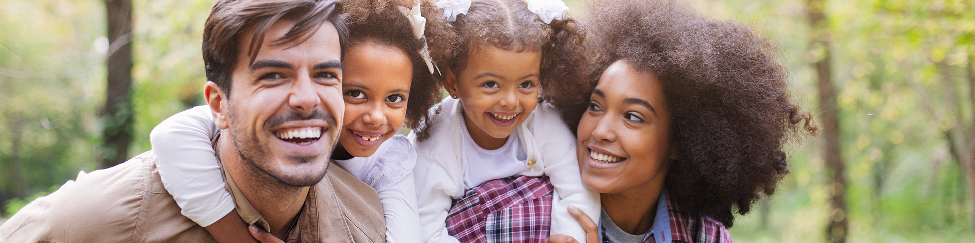 mom and dad with two young girls on their back smiling outdoors 